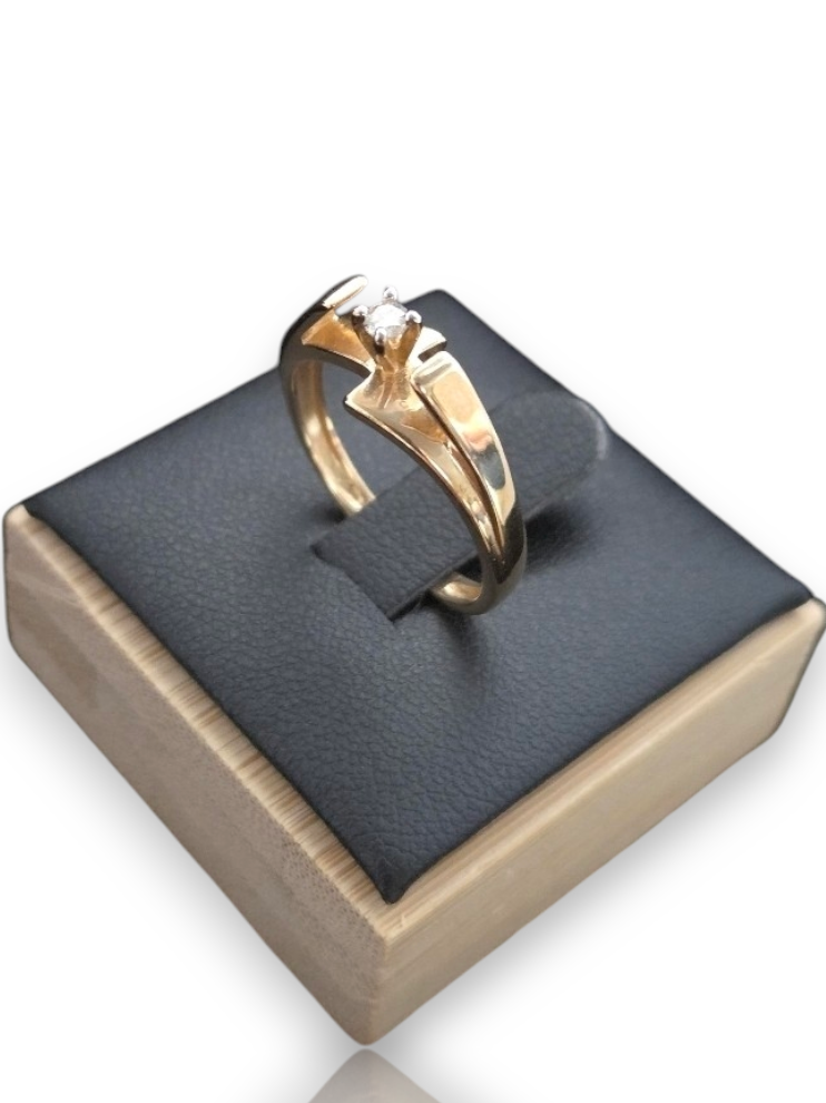 A gold ring with a clear gemstone displayed on a black cushioned wooden jewelry box against a white background