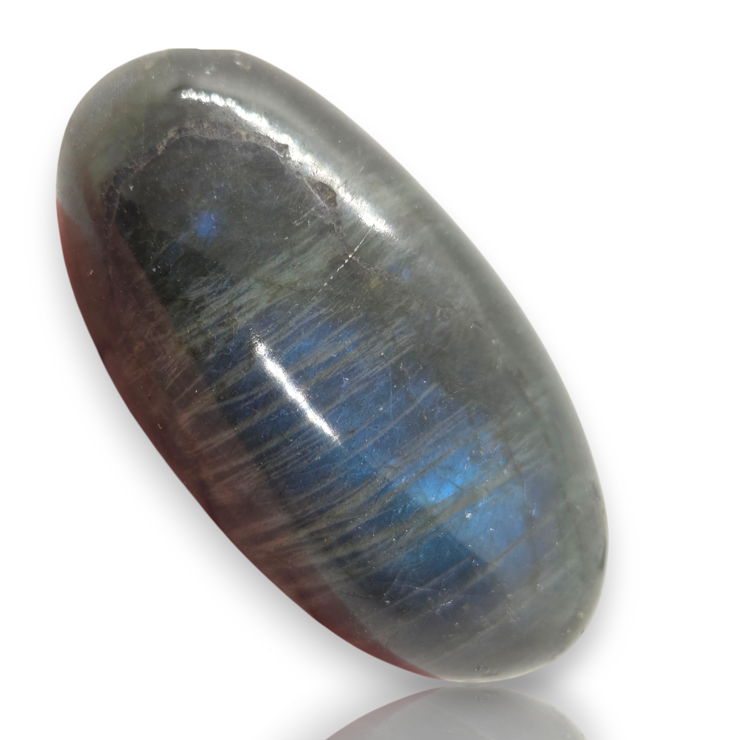 A polished oval labradorite gemstone showing a blue iridescent flash and a reddish-brown edge, displayed on a white background with a reflection below. 