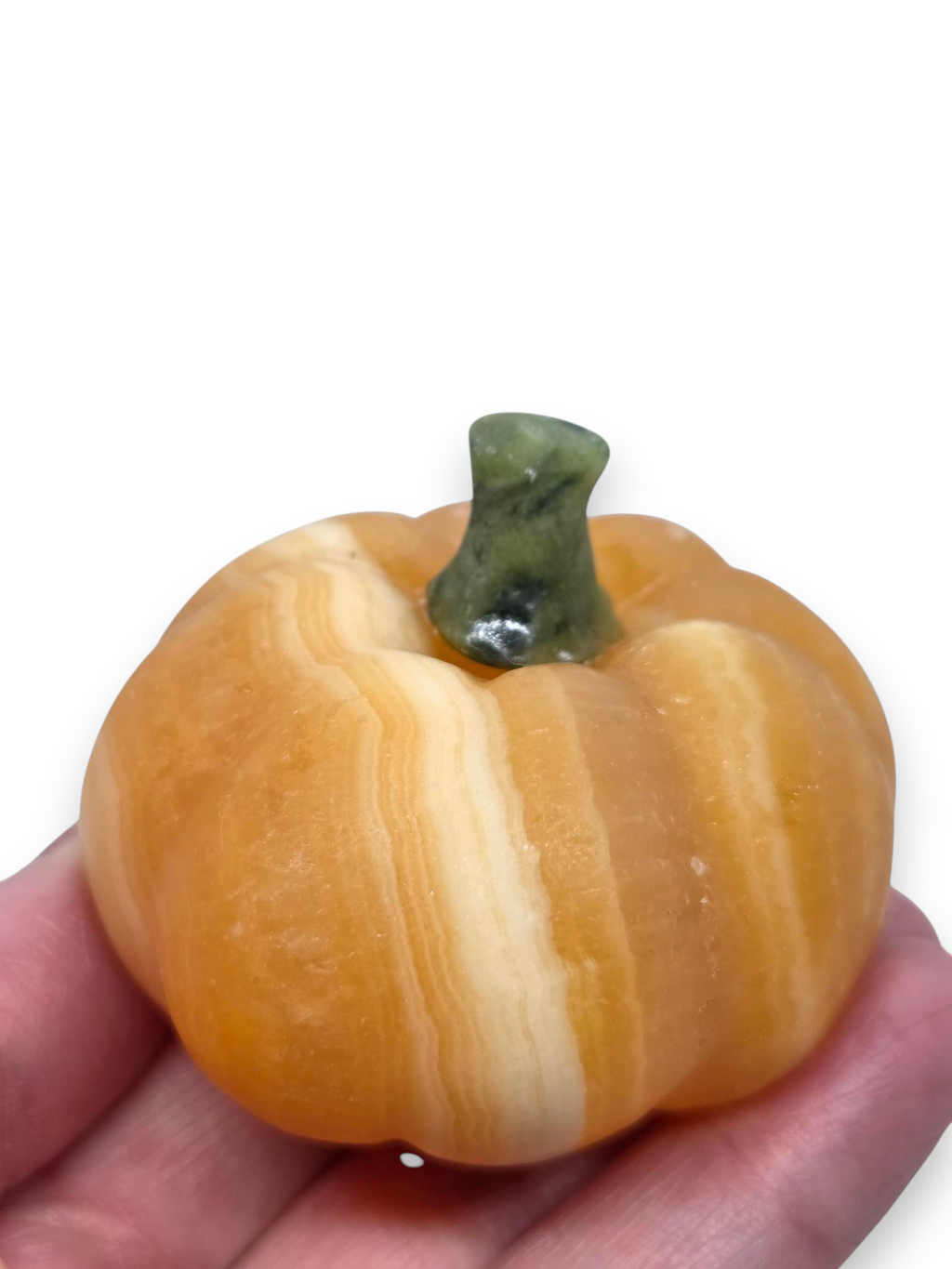 A small decorative pumpkin-shaped object with orange and cream marbled bands and a dark green stem, held in a person's hand against a white background. 