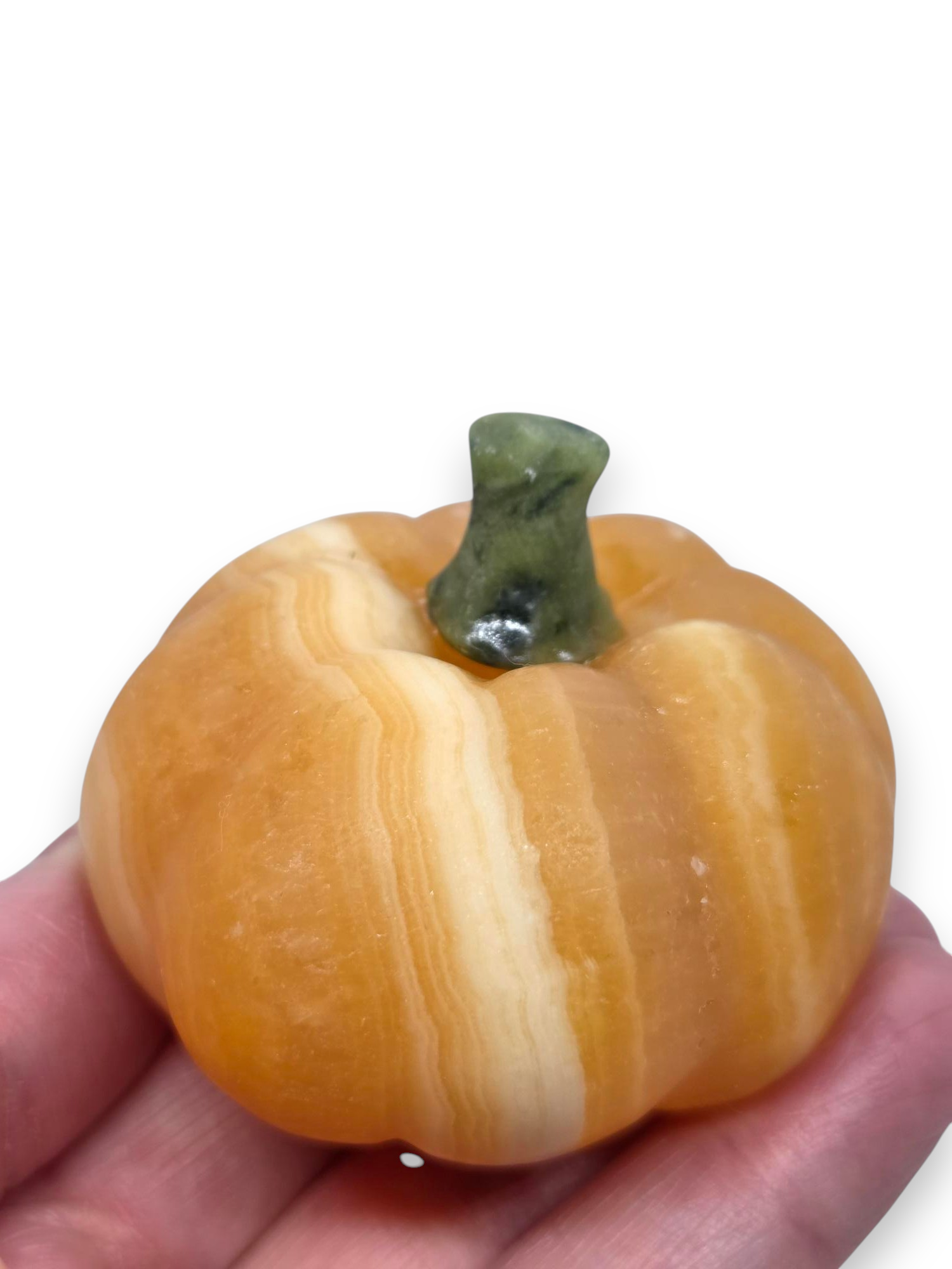 A small decorative pumpkin-shaped object with orange and cream marbled bands and a dark green stem, held in a person's hand against a white background. 