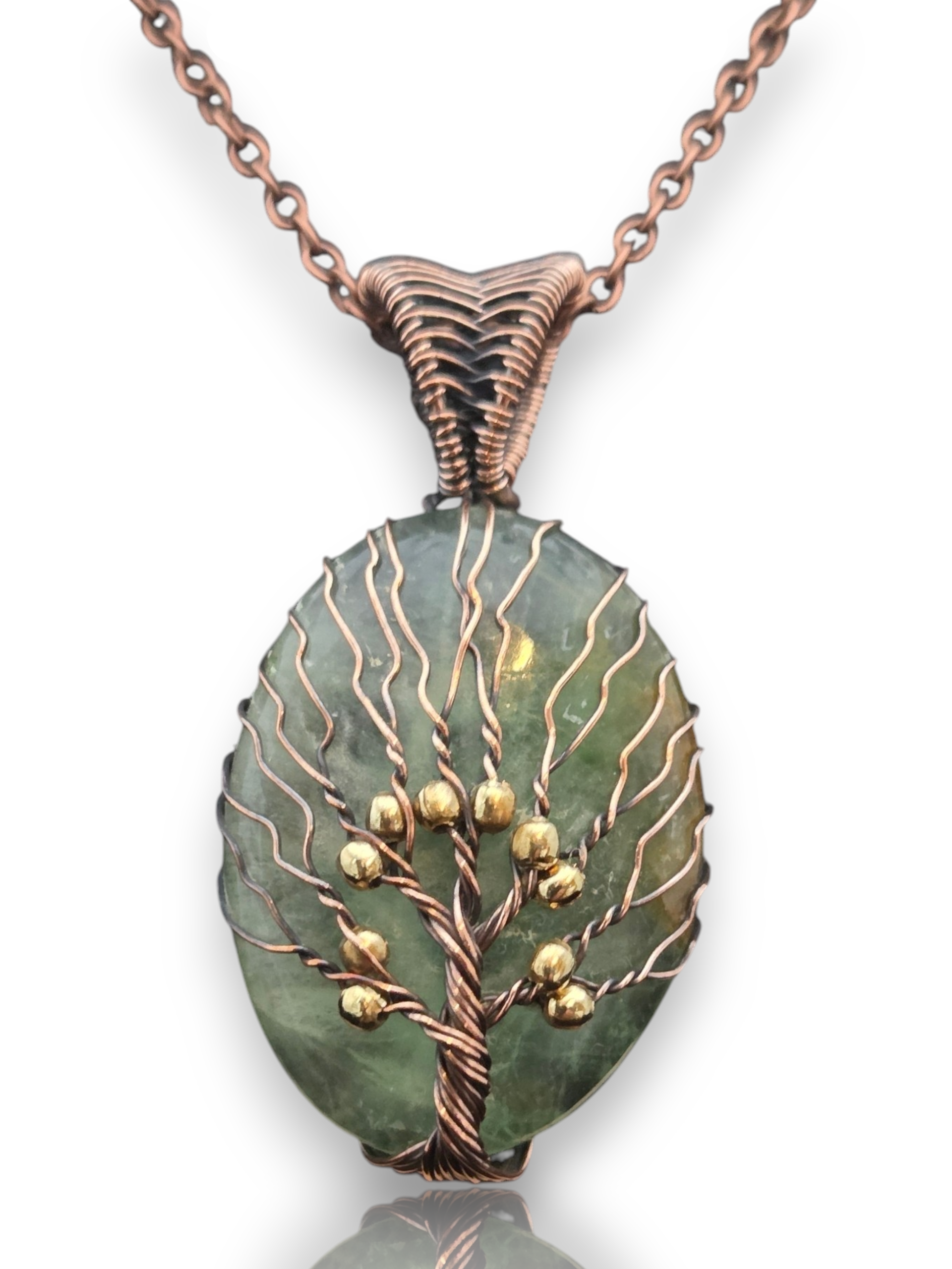 A copper wire-wrapped pendant necklace featuring a green stone cabochon with a tree design and small gold bead accents, shown on a white background with a reflection.