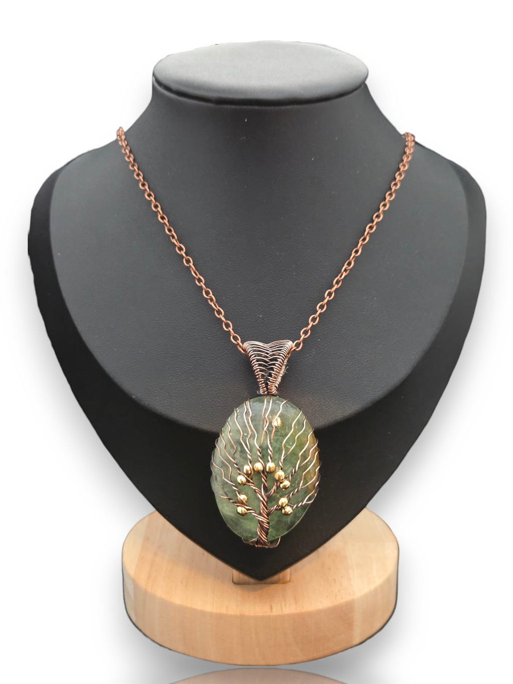 A copper chain necklace with an oval pendant featuring a green and white tree design and small gold berry accents, displayed on a black mannequin bust with a wooden base. 
