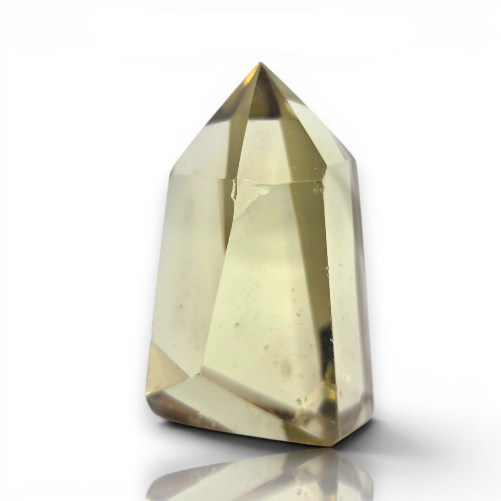 Crystal Chrysalis Haus A faceted crystal point gemstone with a pale yellowish-beige hue, displayed on a clean white background with a soft reflection underneath
