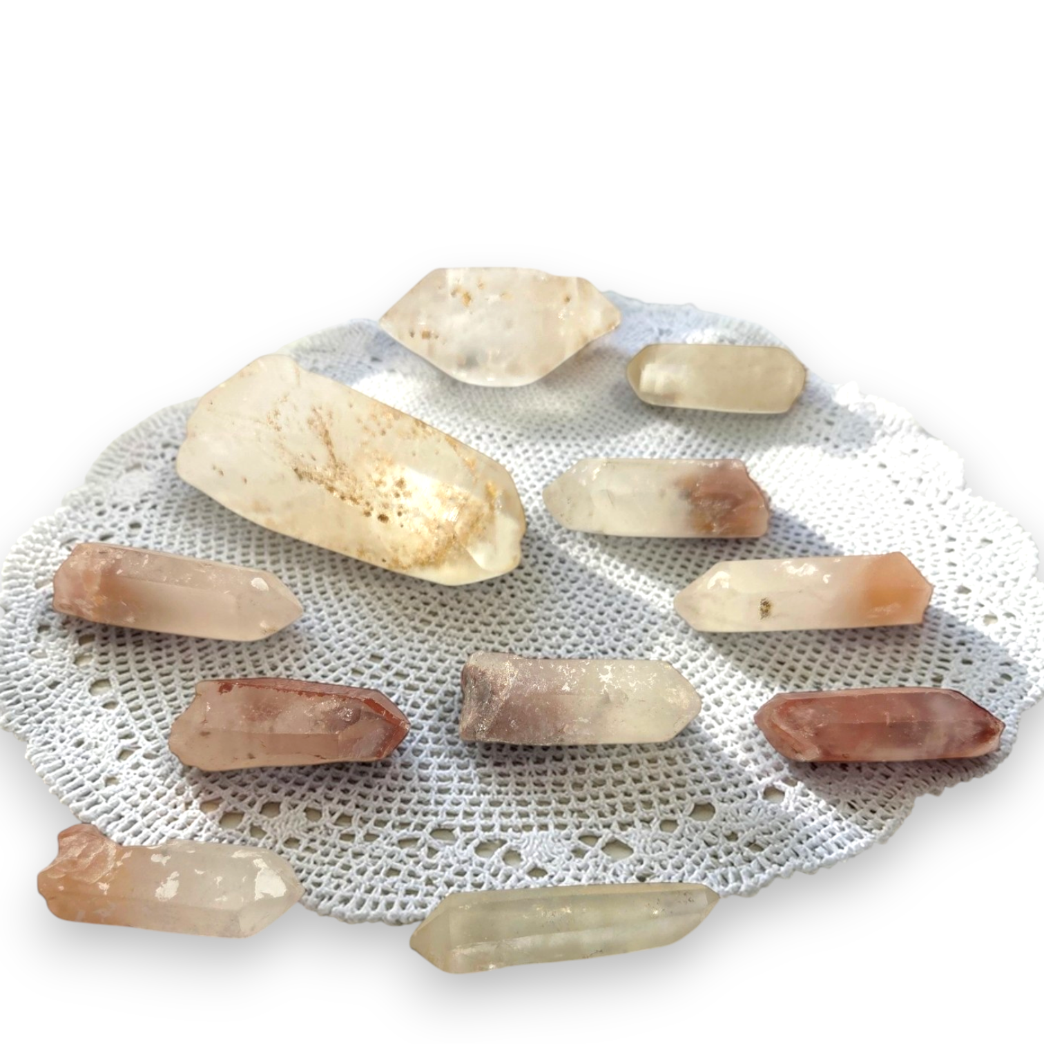 Crystal Chrysalis Haus A collection of natural quartz crystal points in various earthy tones of beige, brown, and translucent white, arranged on a white lace doily 