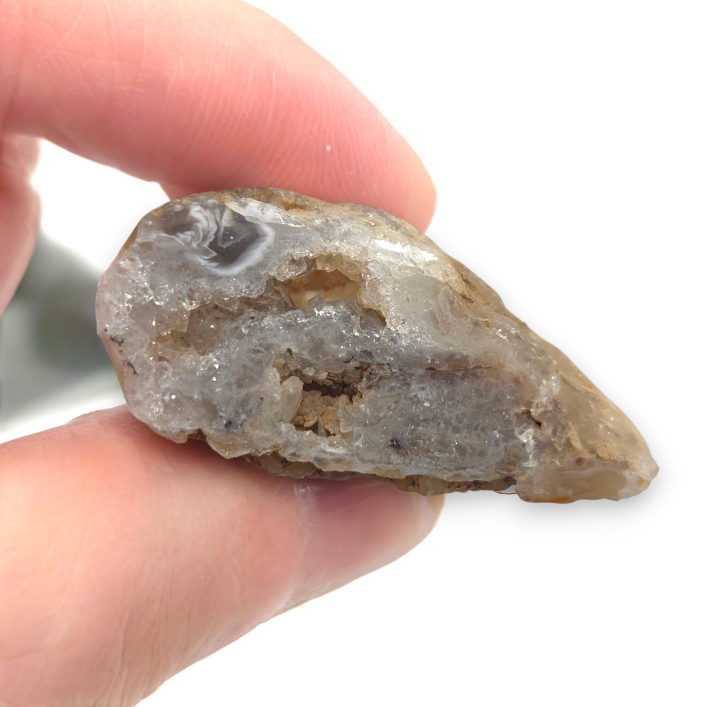 Crystal Chrysalis Haus A hand holding a raw, rough crystal specimen with a gray and white crystalline interior and a brown outer matrix, shown against a white background 