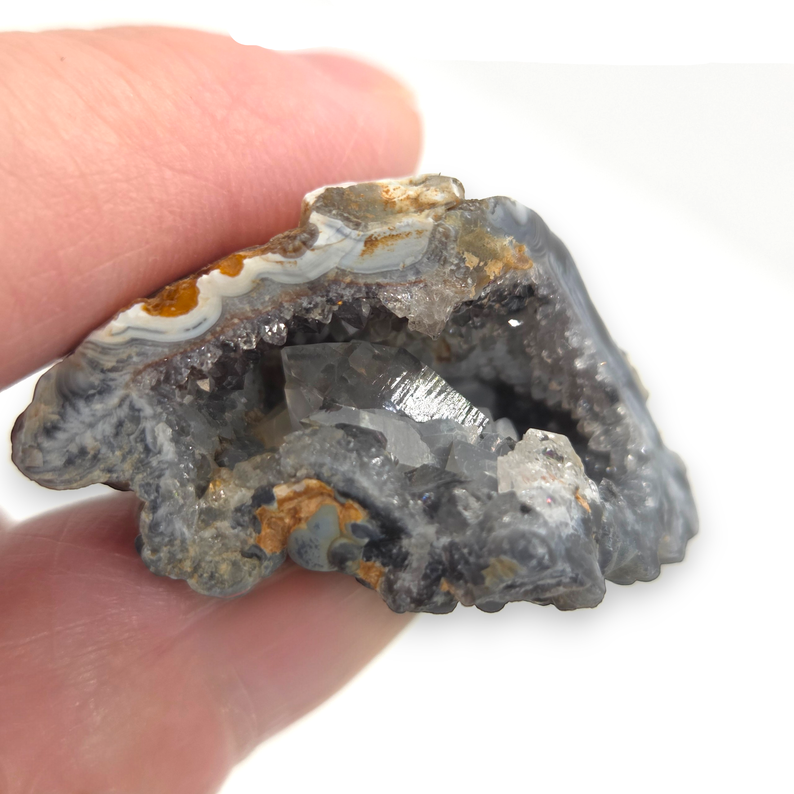 Crystal Chrysalis Haus A hand holding a rough agate crystal geode specimen with gray agate walls and clear crystals inside, against a white background 