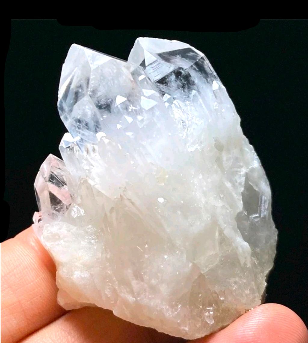 Crystal Chrysalis Haus  A hand holding a large clear quartz crystal cluster against a black background