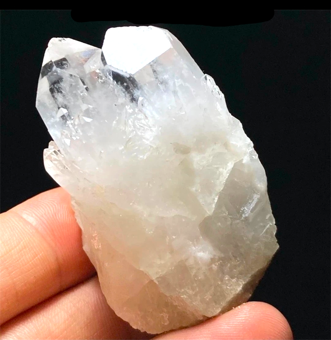 Crystal Chrysalis Haus  A raw clear quartz crystal cluster held in a person's hand against a black background