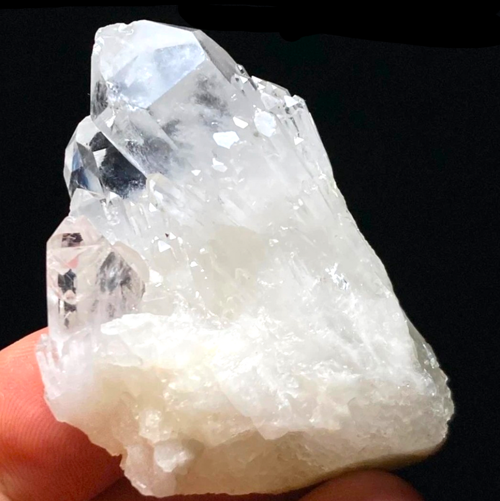 Crystal Chrysalis Haus A raw white and clear crystal cluster held in a person's hand against a black background