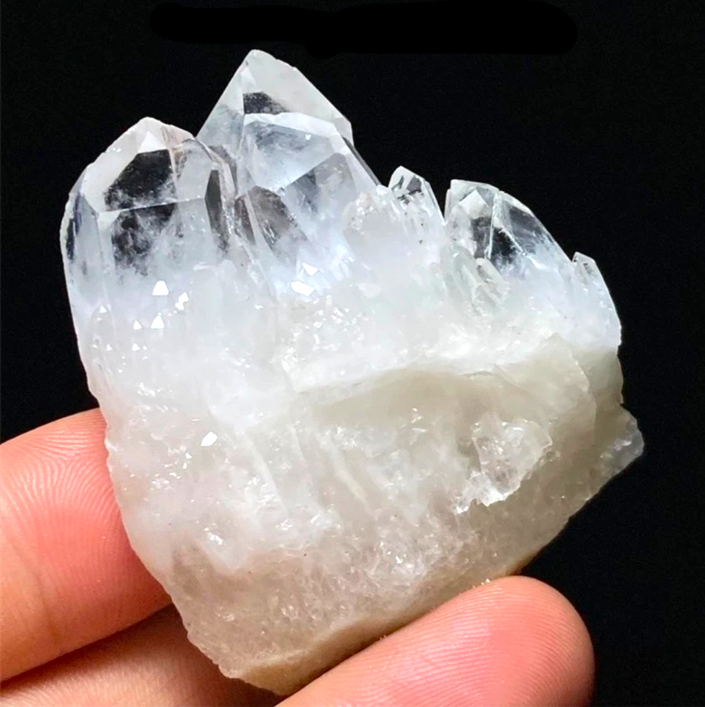 Crystal Chrysalis Haus  A hand holding a raw white crystal cluster with multiple sharp points against a black background