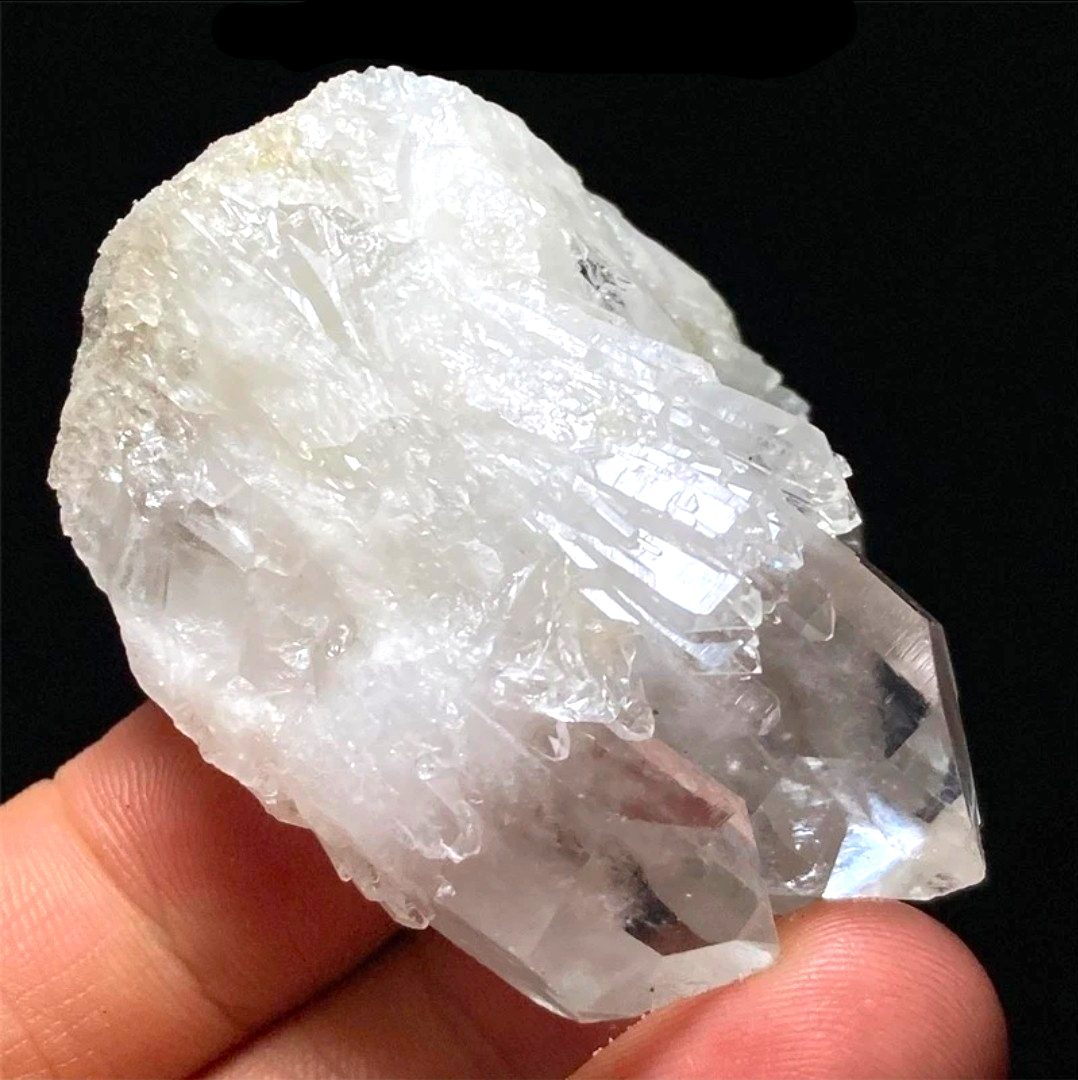 Crystal Chrysalis Haus  A hand holding a large, rough, semi-translucent white and clear crystal cluster against a solid black background