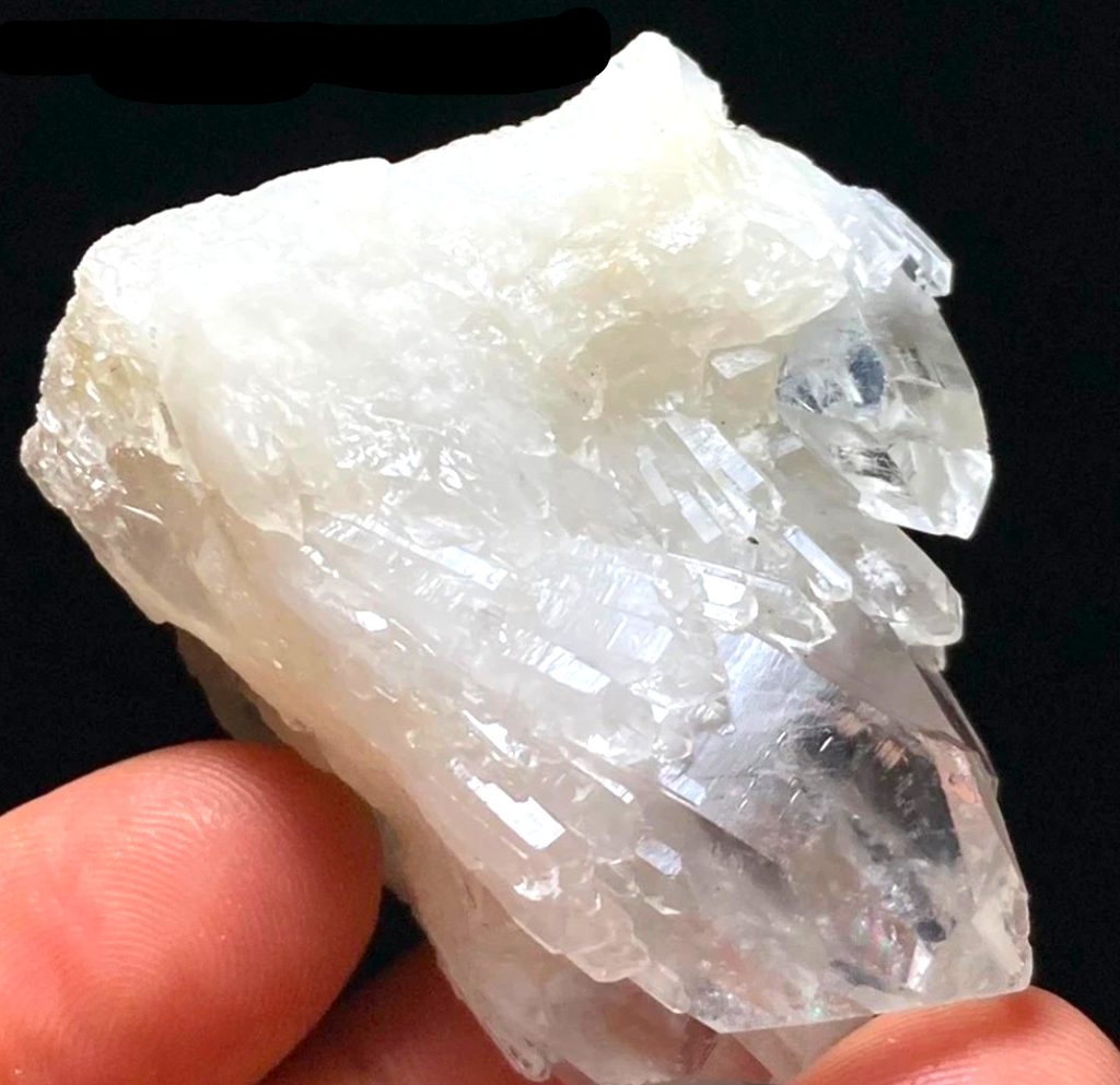 Crystal Chrysalis Haus  A raw, rough white quartz crystal cluster held in a person's fingers against a solid black background