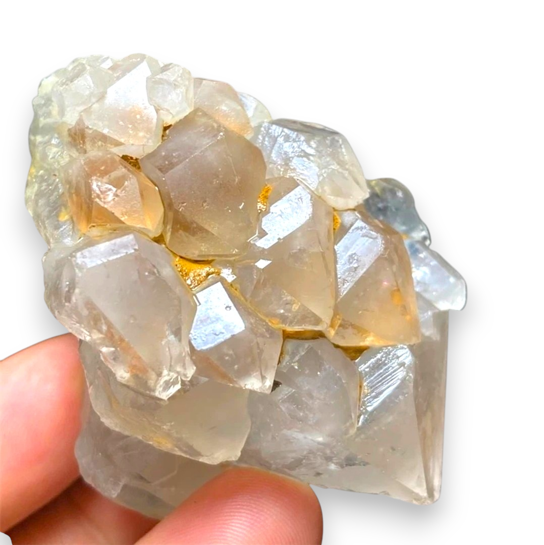 Crystal Chrysalis Haus A hand holding a raw crystal cluster with translucent pale gray and milky white stones, some showing subtle golden warmth, on a white background