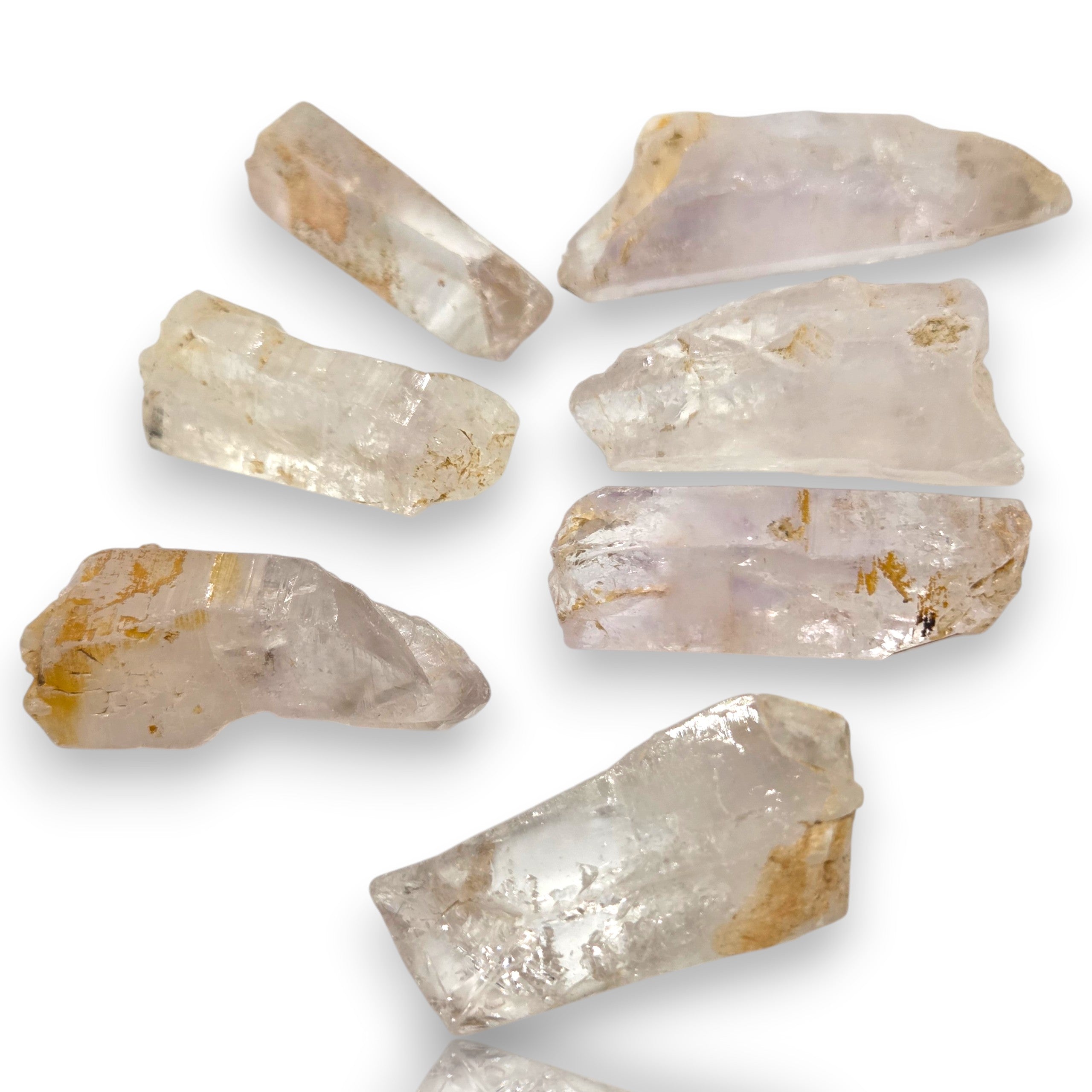 Crystal Chrysalis Haus Seven raw, rough crystal mineral specimens with natural jagged edges, showing translucent white and pale lavender hues with subtle golden-brown inclusions, arranged on a plain white background.