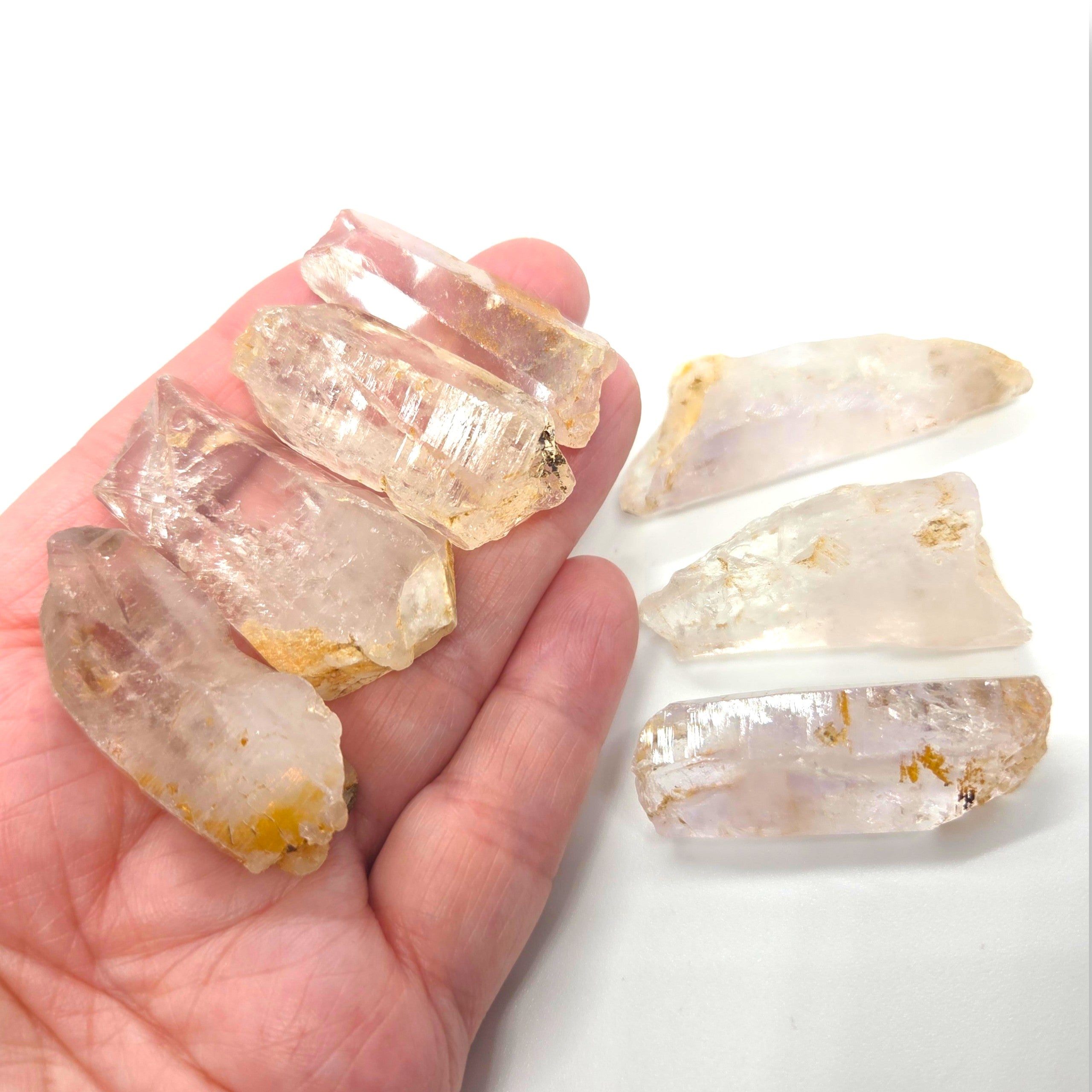 Crystal Chrysalis Haus Five raw, translucent quartz crystal points with natural golden-yellow inclusions, shown resting on a white surface with a hand holding three of them for scale.
