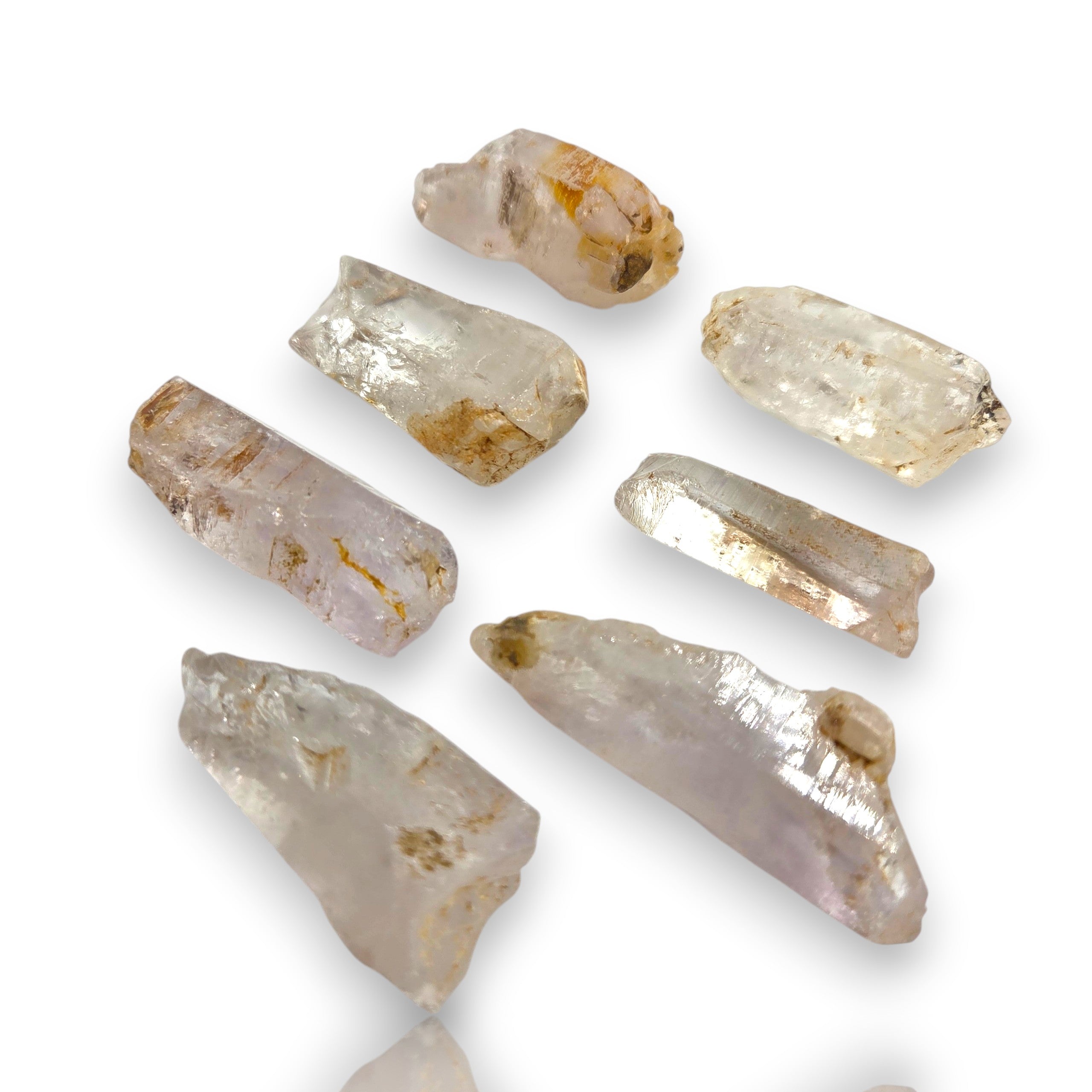 Crystal Chrysalis Haus Seven raw, rough crystal points of varying shapes and sizes, displaying natural translucent qualities with subtle brown and gold inclusions, arranged on a clean white background.