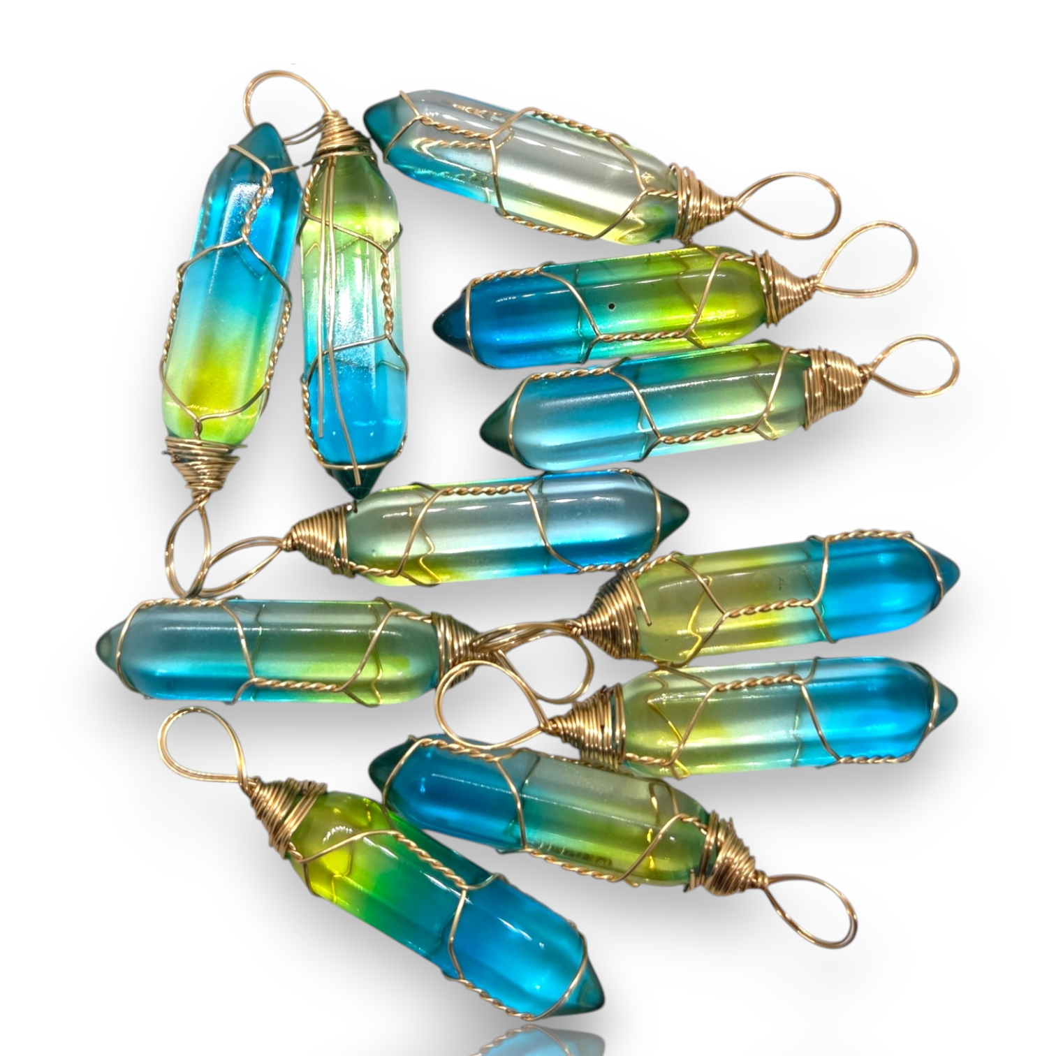 Crystal Chrysalis Haus Nine blue and green gradient crystal point pendants with gold wire wrapping, arranged on a clean white background.
