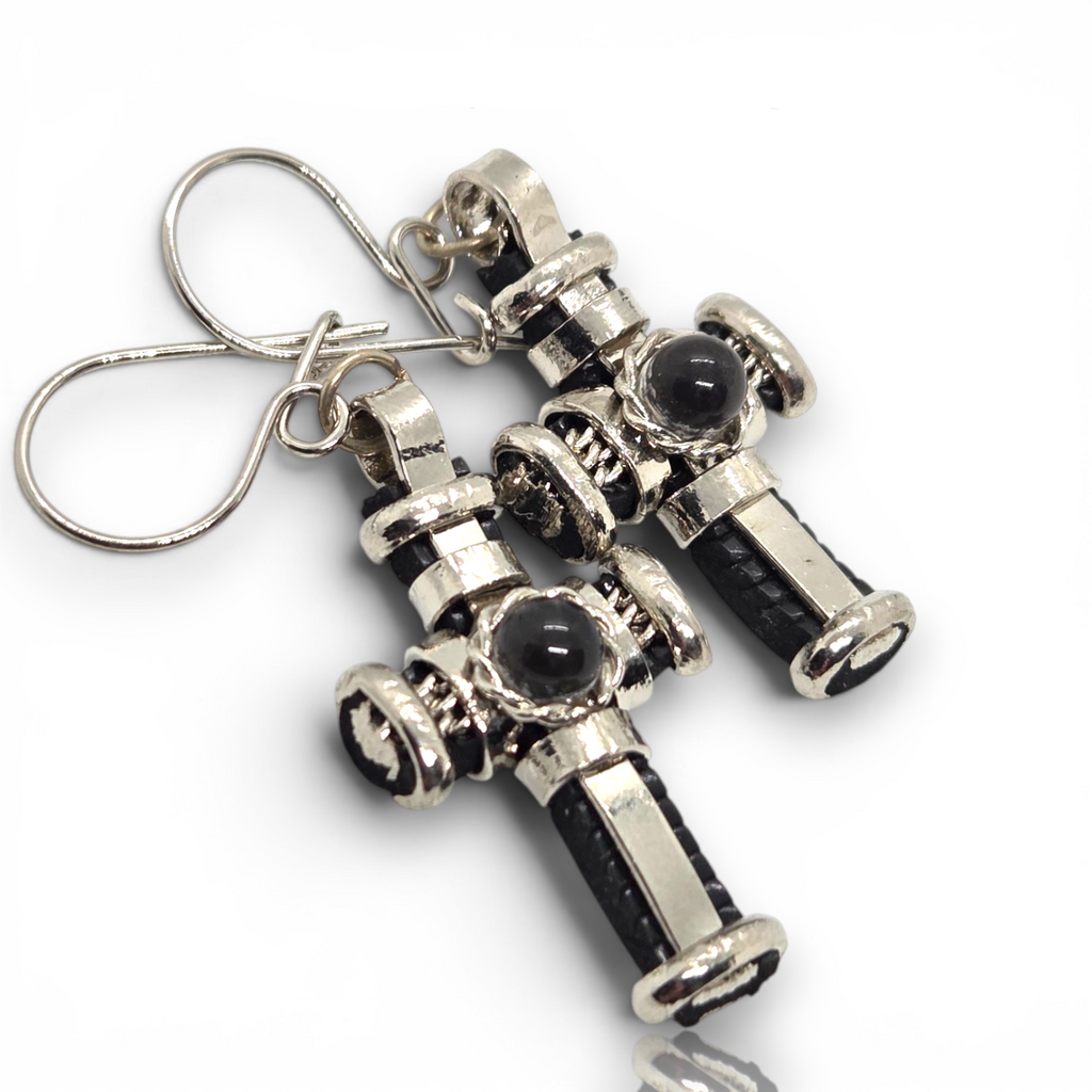 Crystal Chrysalis Haus A pair of silver-toned cross-shaped earrings with black textured inlays and oval black stone centers, attached to silver fishhook ear wires, shown on a white background.