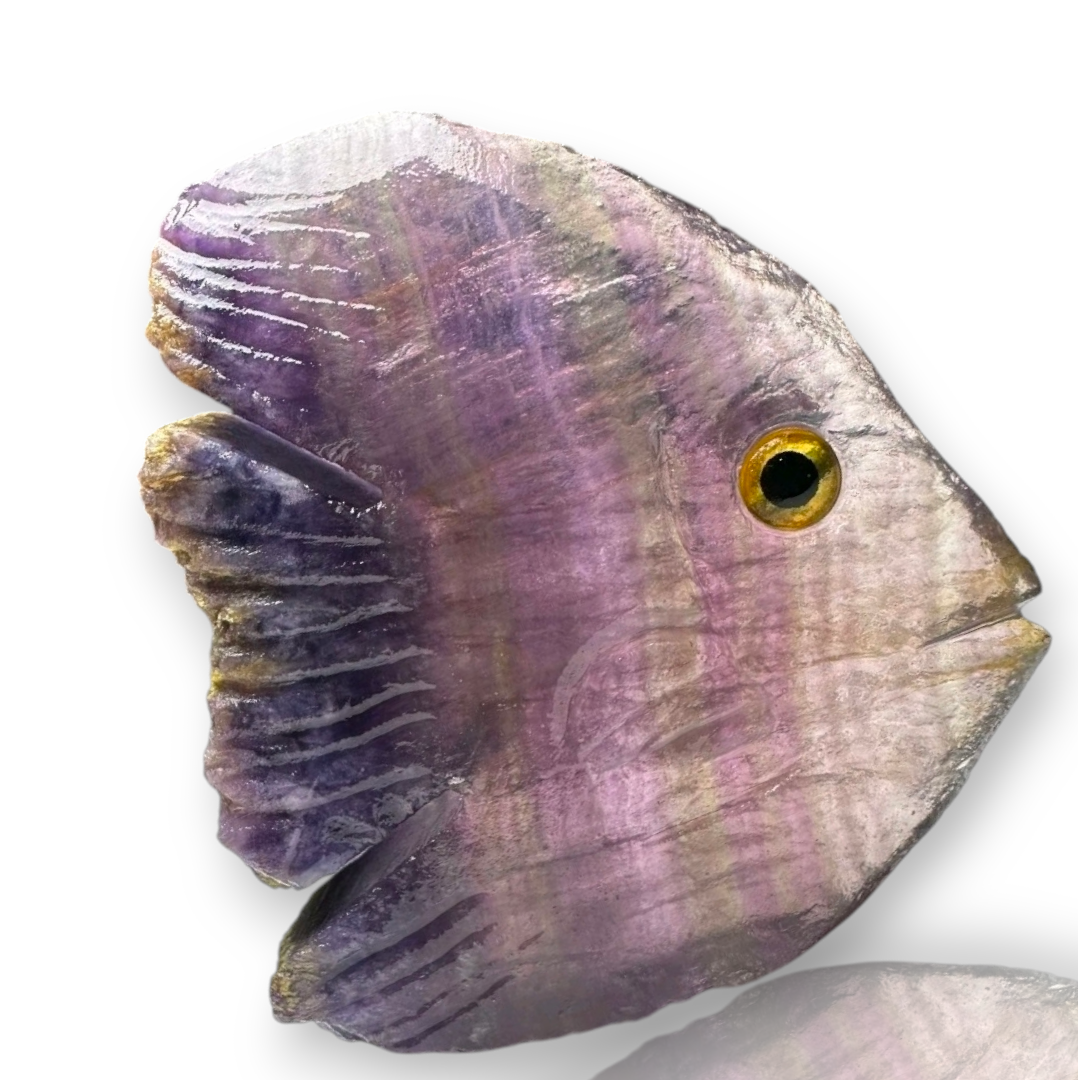 Crystal Chrysalis Haus A carved fish-shaped object, likely a decorative sculpture or pendant, made from purple and lavender marbled stone with a textured surface and a carved eye