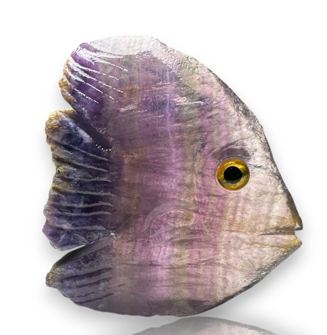 Crystal Chrysalis Haus A fish-shaped gemstone bead with purple, lavender, and gray banded striations, featuring a realistic gold eye