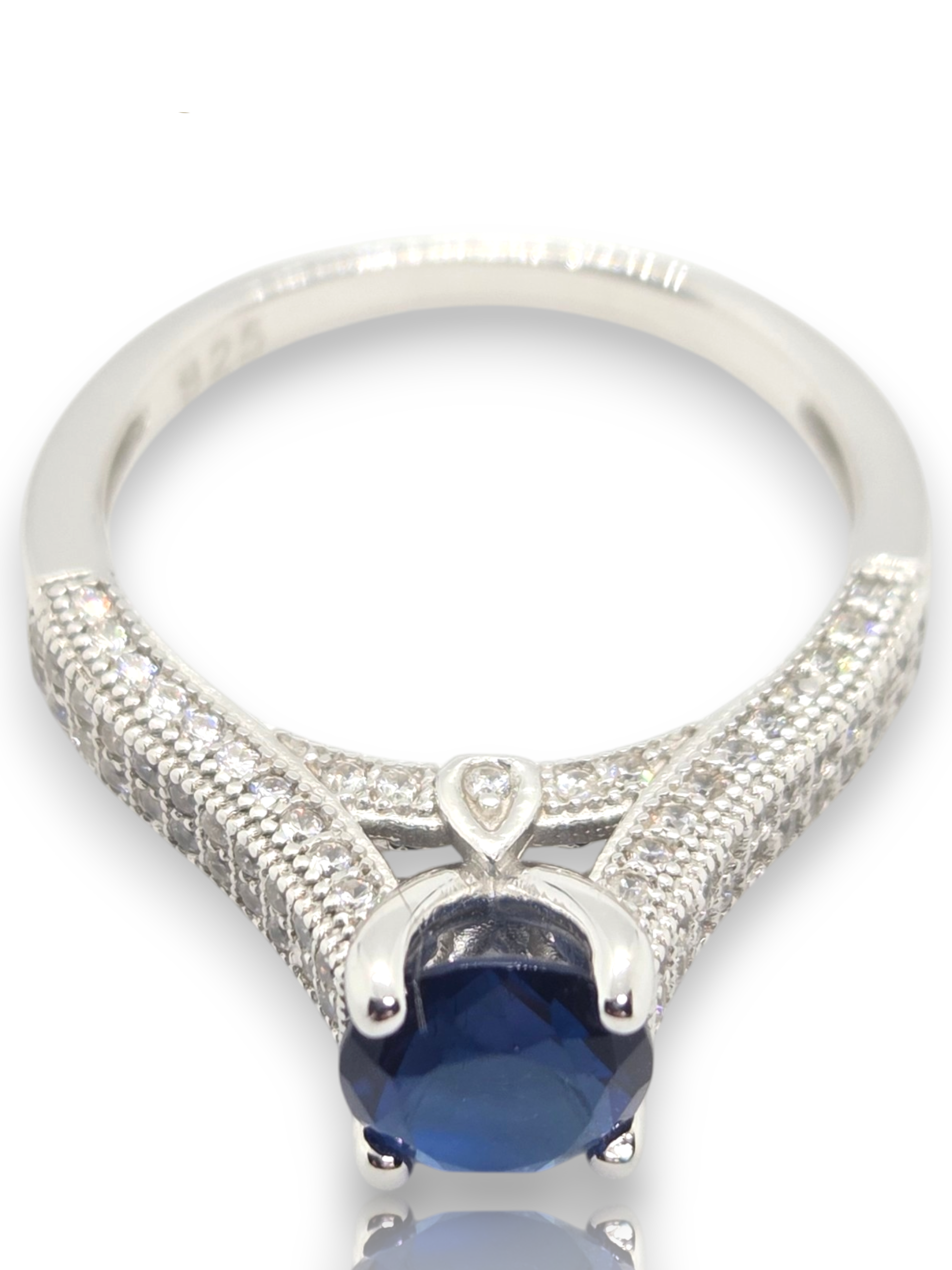 Crystal Chrysalis Haus  A silver-toned ring with a large oval deep blue gemstone and pavé-set clear stones along the band, shown on a white background 