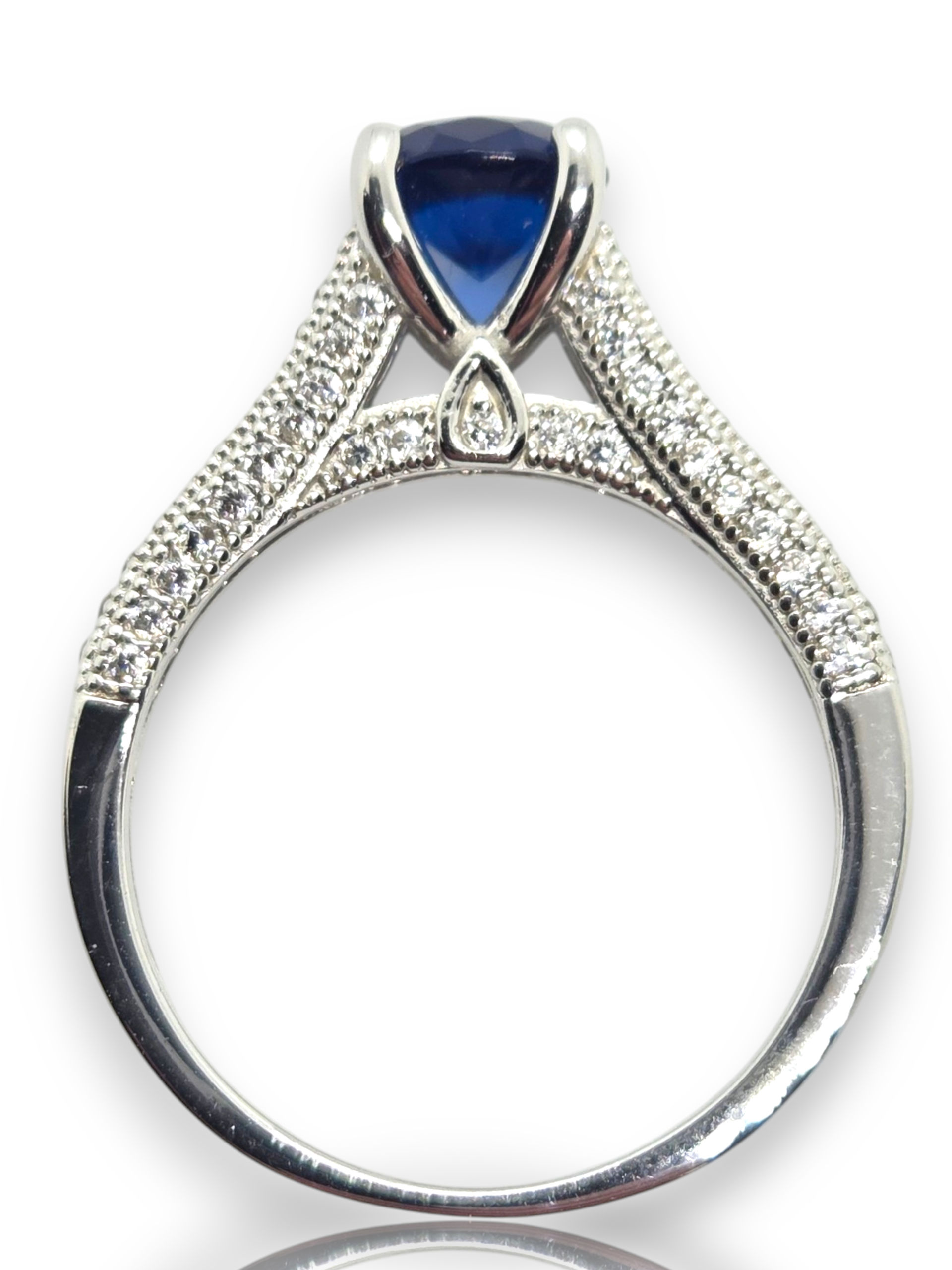 Crystal Chrysalis Haus A silver-toned split-shank ring featuring a deep blue teardrop-shaped center stone and pavé-set clear stones along the shoulders, shown on a white background 