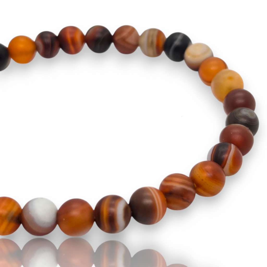 Crystal Chrysalis Haus A beaded stretch bracelet made of polished round beads in earthy tones of orange, brown, black, white, and tan, arranged in a circle on a white background.