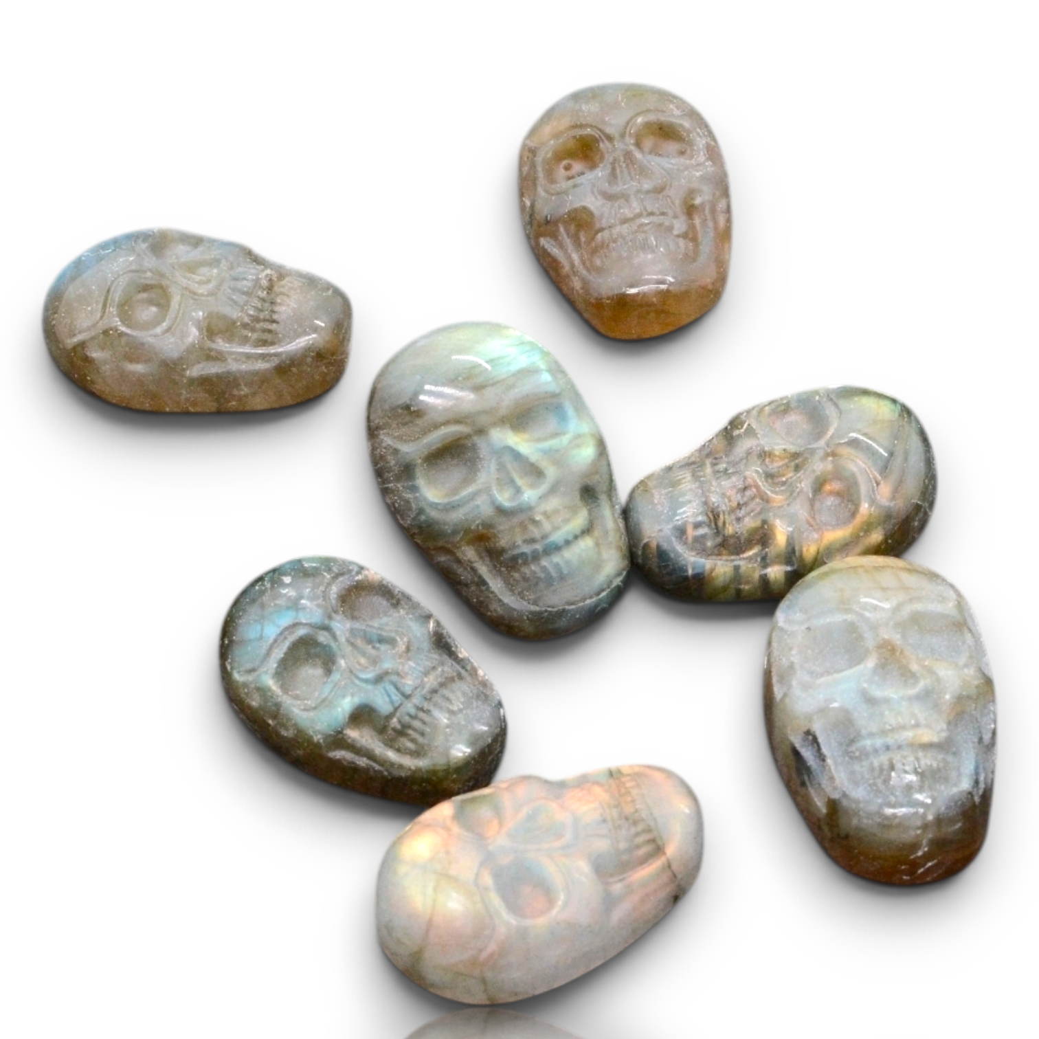 Seven polished skull-shaped gemstones with an iridescent opal-like sheen, arranged on a plain white background. 