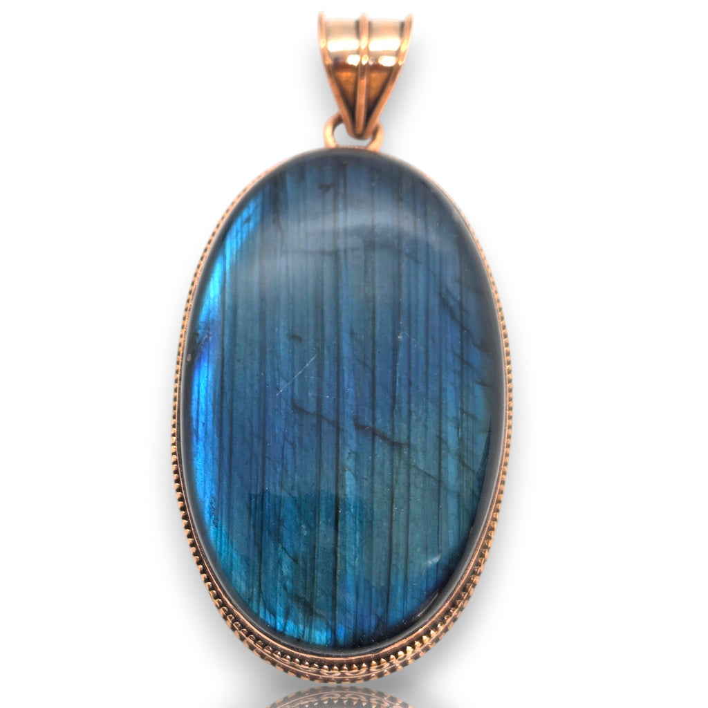 Crystal Chrysalis Haus An oval labradorite pendant in a rose gold bezel setting, featuring a vibrant blue and green iridescent flash on a white background.