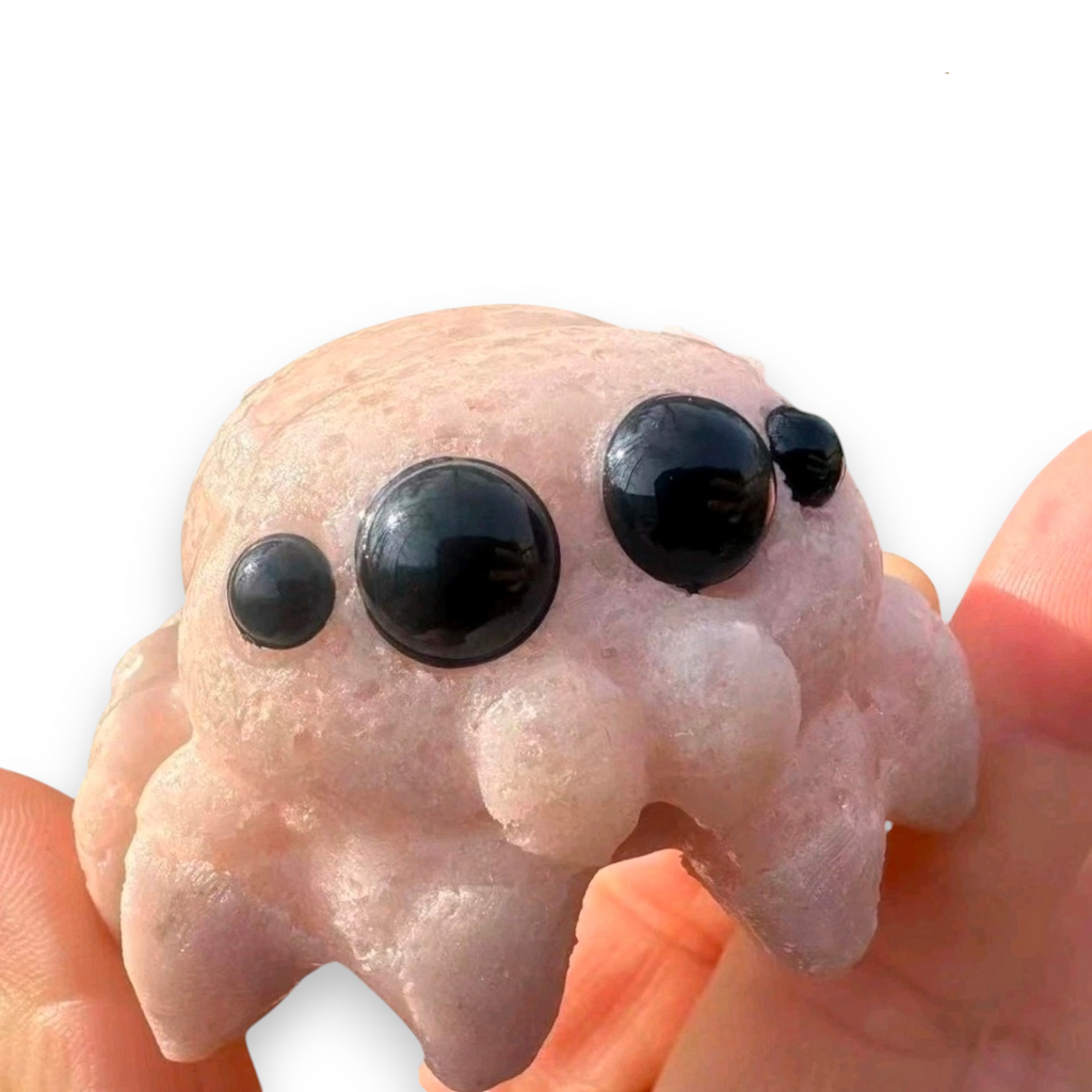A pink cat-shaped carved object with three glossy black eyes, shown being held in human hands against a white background