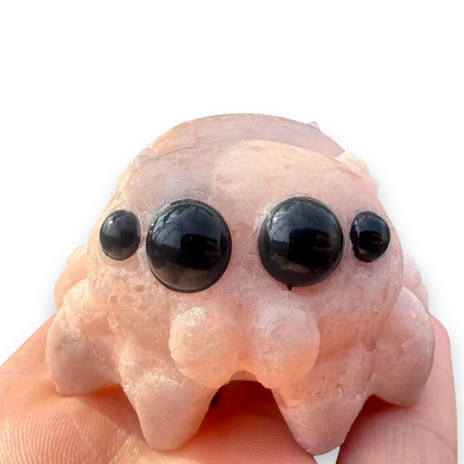 A pink stone creature figurine with three large black eyes and smaller side eyes, held in a hand against a white background
