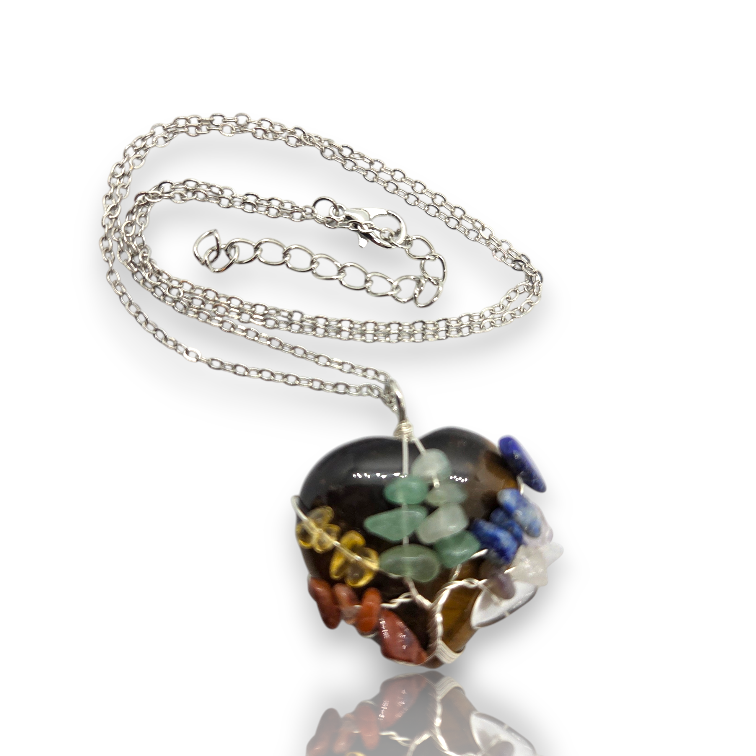 Crystal Chrysalis Haus A silver chain necklace with a heart-shaped pendant made of multiple colored stones and green leaf details, shown on a white background with a reflection below.