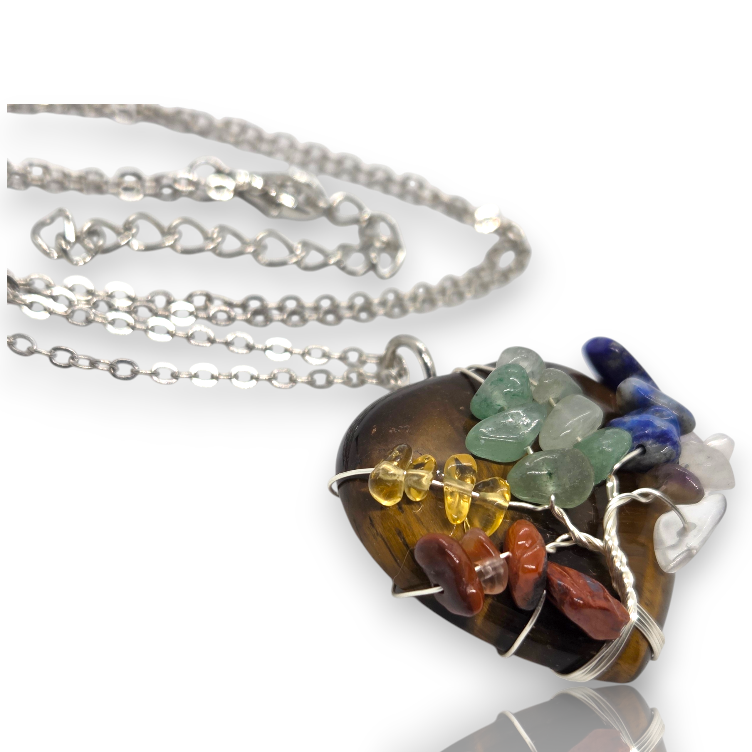 Crystal Chrysalis Haus A silver chain necklace with a heart-shaped pendant made from polished tiger's eye and wrapped with multicolored raw stone chips, shown on a white background with a soft reflection.