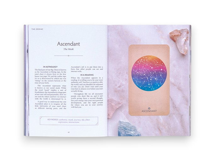 An open book spread showing a page about the Ascendant with text on the left and a colorful natal chart card on the right, styled with crystals on a pale marble background.