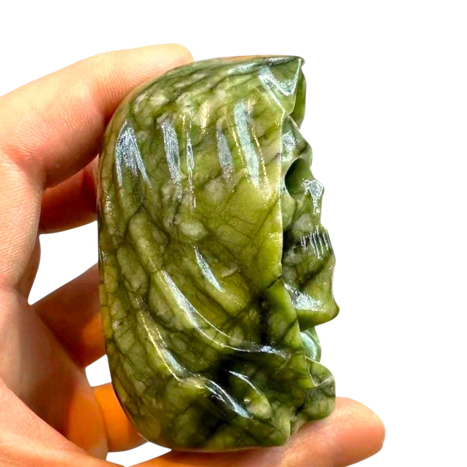 A hand holds a polished green carved stone sculpture with a leaf-like pattern, shown against a plain white background 