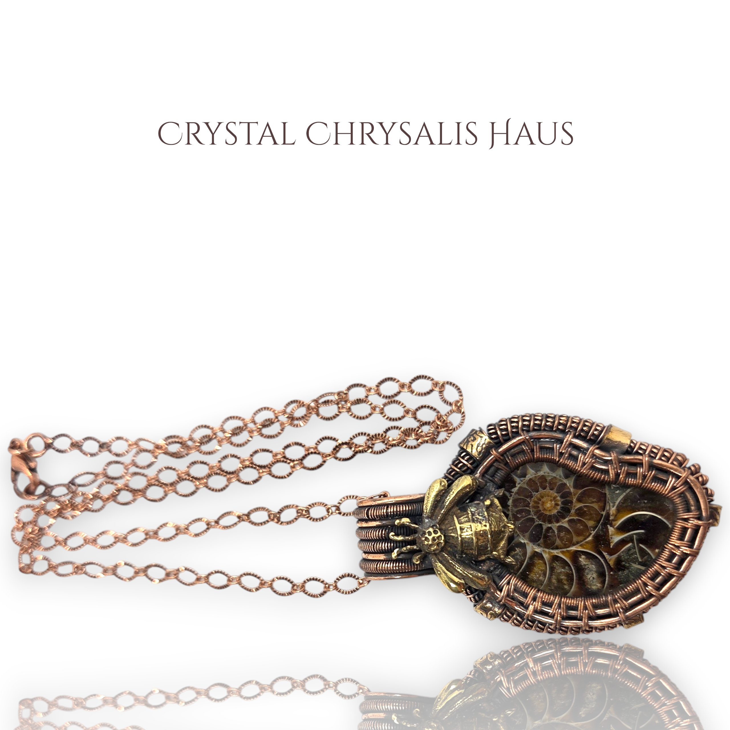 A steampunk-style ammolite pendant necklace with rose gold and bronze metalwork, featuring a detailed spiral ammolite center, a small skull accent, and a chain, shown on a white background with the brand name 'CRYSTAL CHRYsalis HAUS' above.