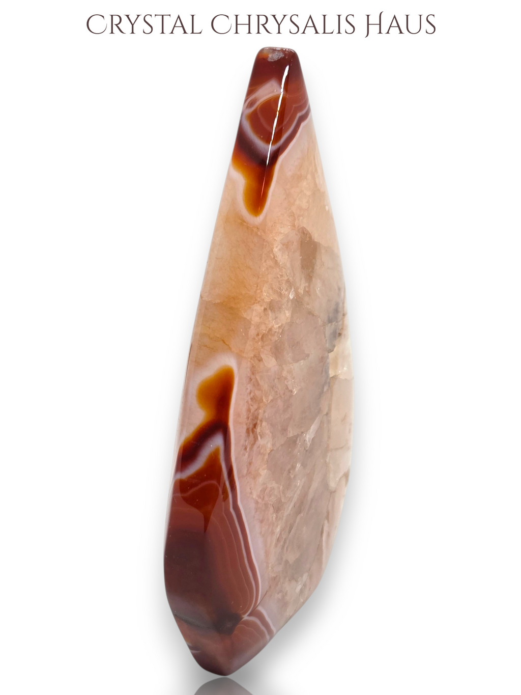 A polished teardrop-shaped crystal pendant with natural banding in shades of brown, beige, and translucent cream, displayed on a clean white background with 'CRYSTAL CHRYSALIS HAUS' text at the top.