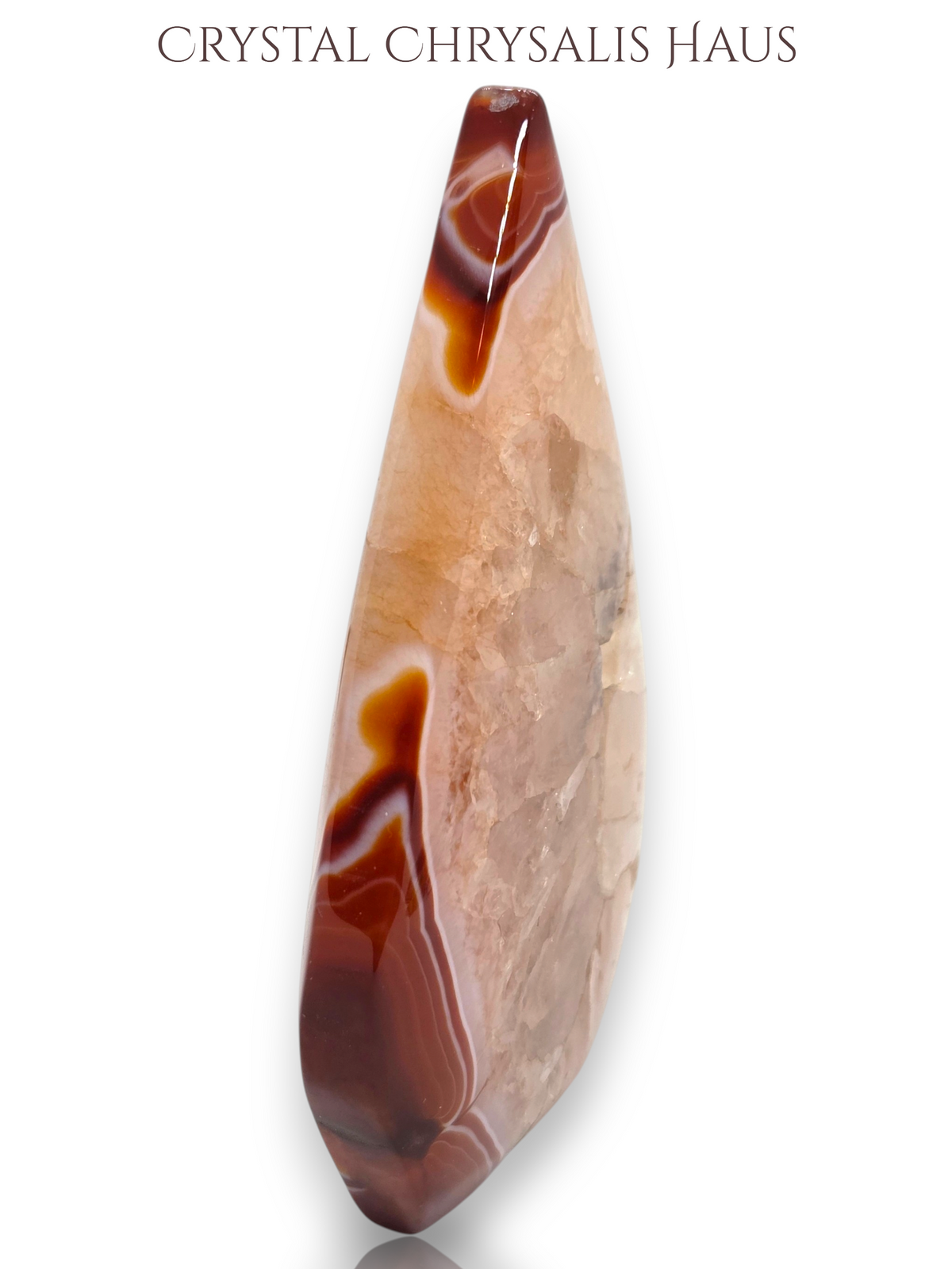 A polished teardrop-shaped crystal pendant with natural banding in shades of brown, beige, and translucent cream, displayed on a clean white background with 'CRYSTAL CHRYSALIS HAUS' text at the top.
